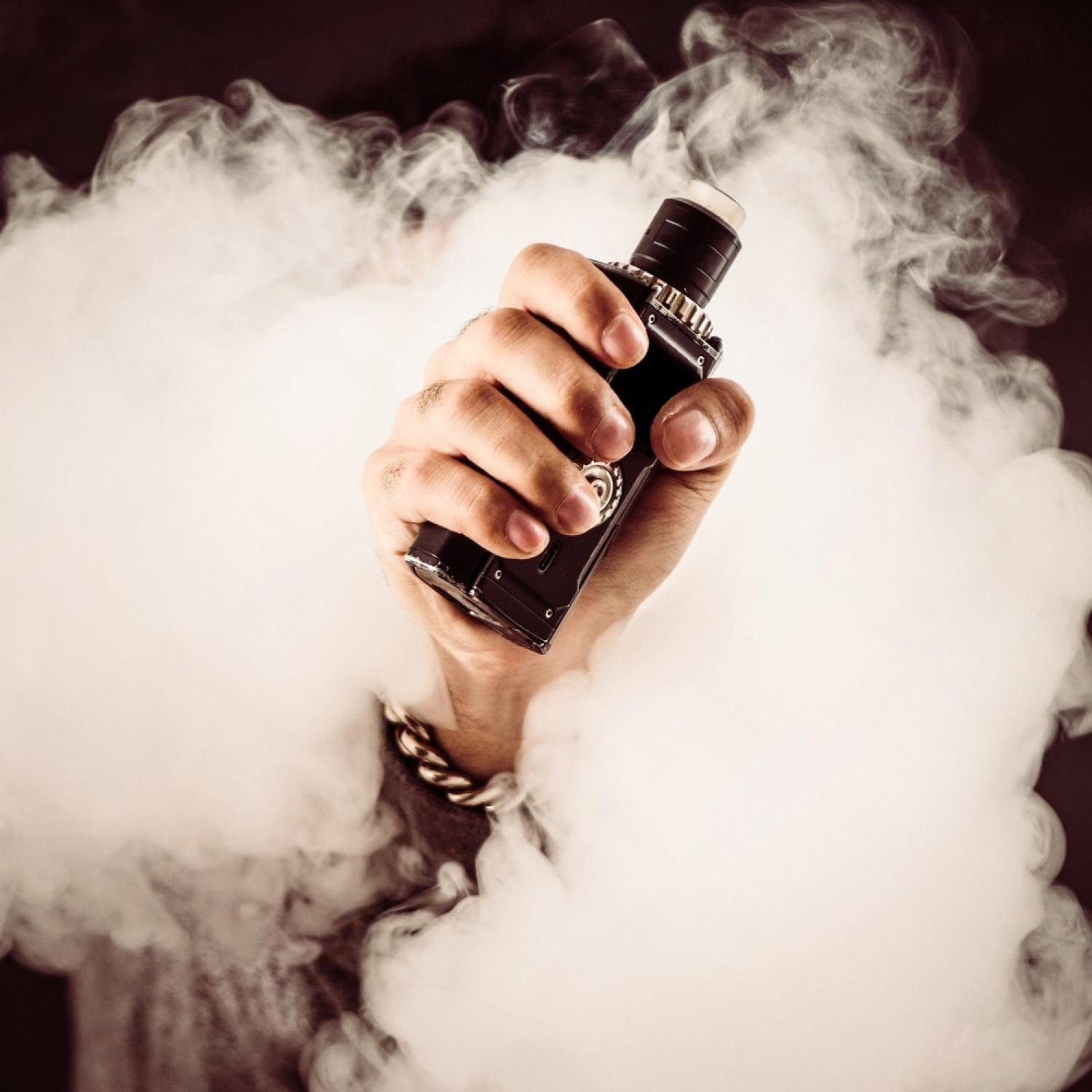 Hand holding a vape mod surrounded by a thick cloud of vapour produced by heated e-liquid