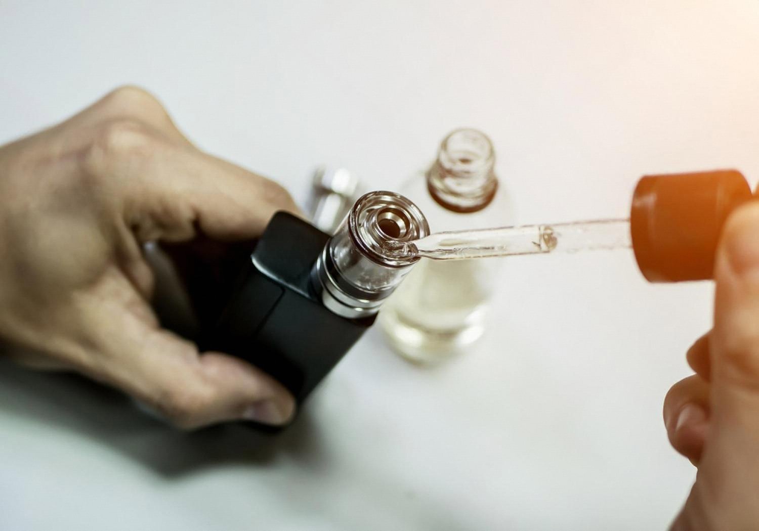 Person refilling a vape tank with e-liquid using a dropper bottle